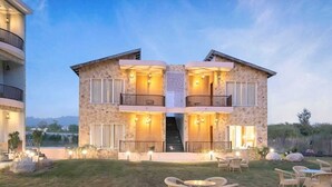 A two-story stone building with balconies, outdoor seating, and a staircase leading to the upper floor. - Delight The Lavish Loft Corbett (Kaladhungi)