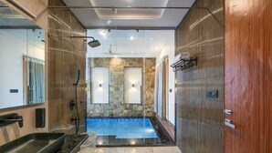 A modern bathroom with a glass-enclosed shower, a stone wall, and a wooden vanity. - Delight The Lavish Loft Corbett (Kaladhungi)