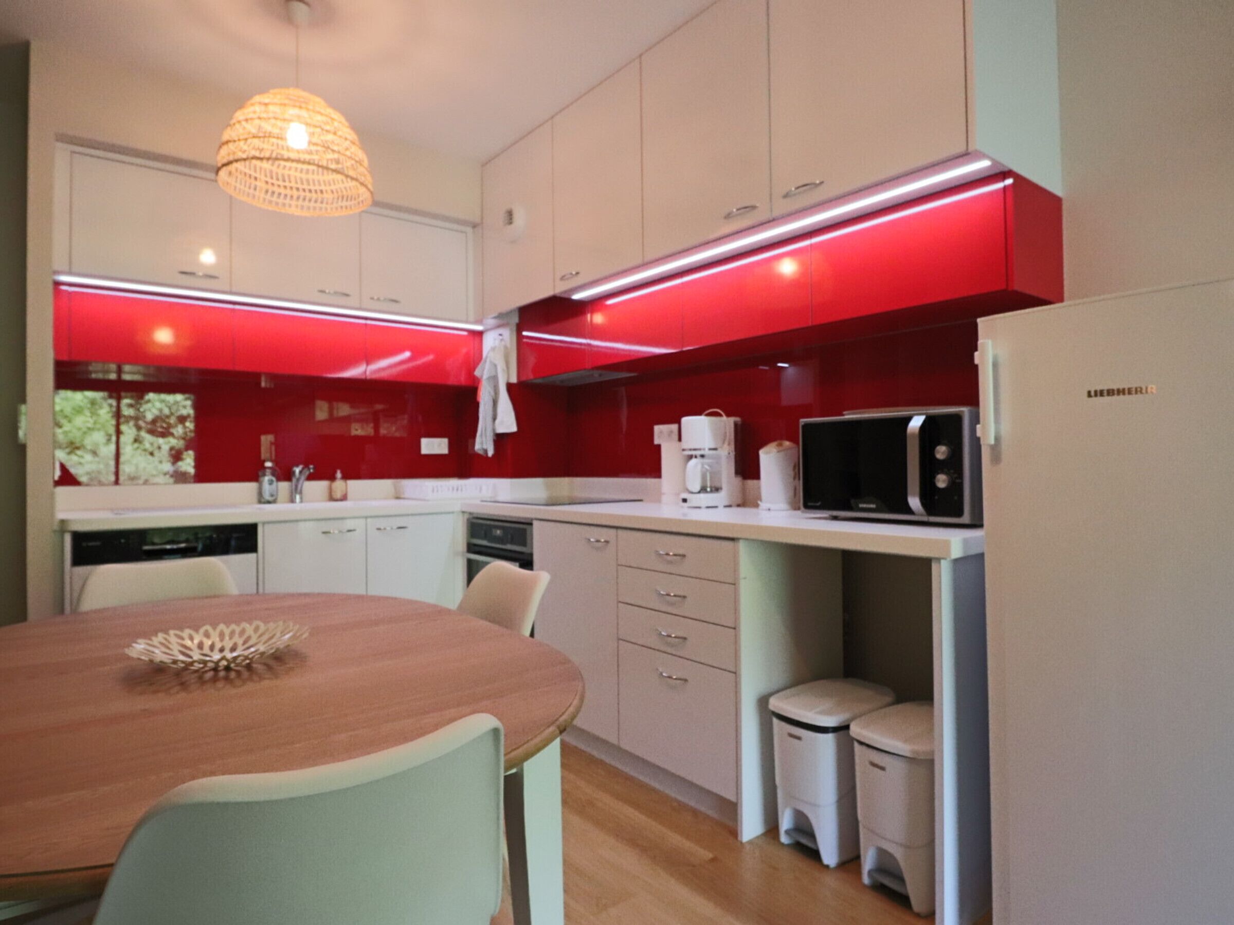Una cocina moderna con gabinetes blancos, un salpicadero rojo y un microondas integrado.