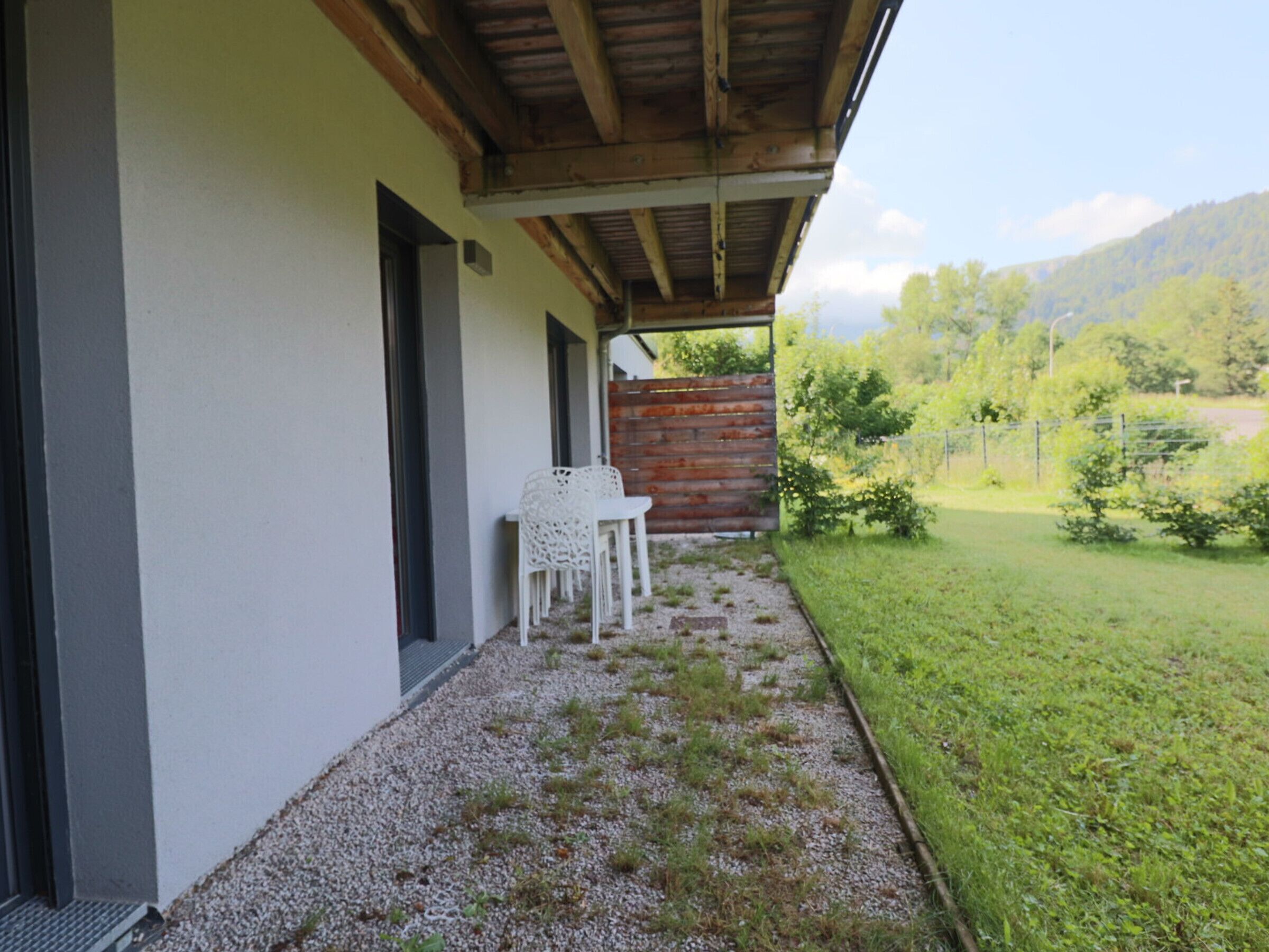 Un espacio al aire libre cubierto con un sendero de grava que conduce a una silla y una mesa blancas, rodeado de césped y una valla de madera.