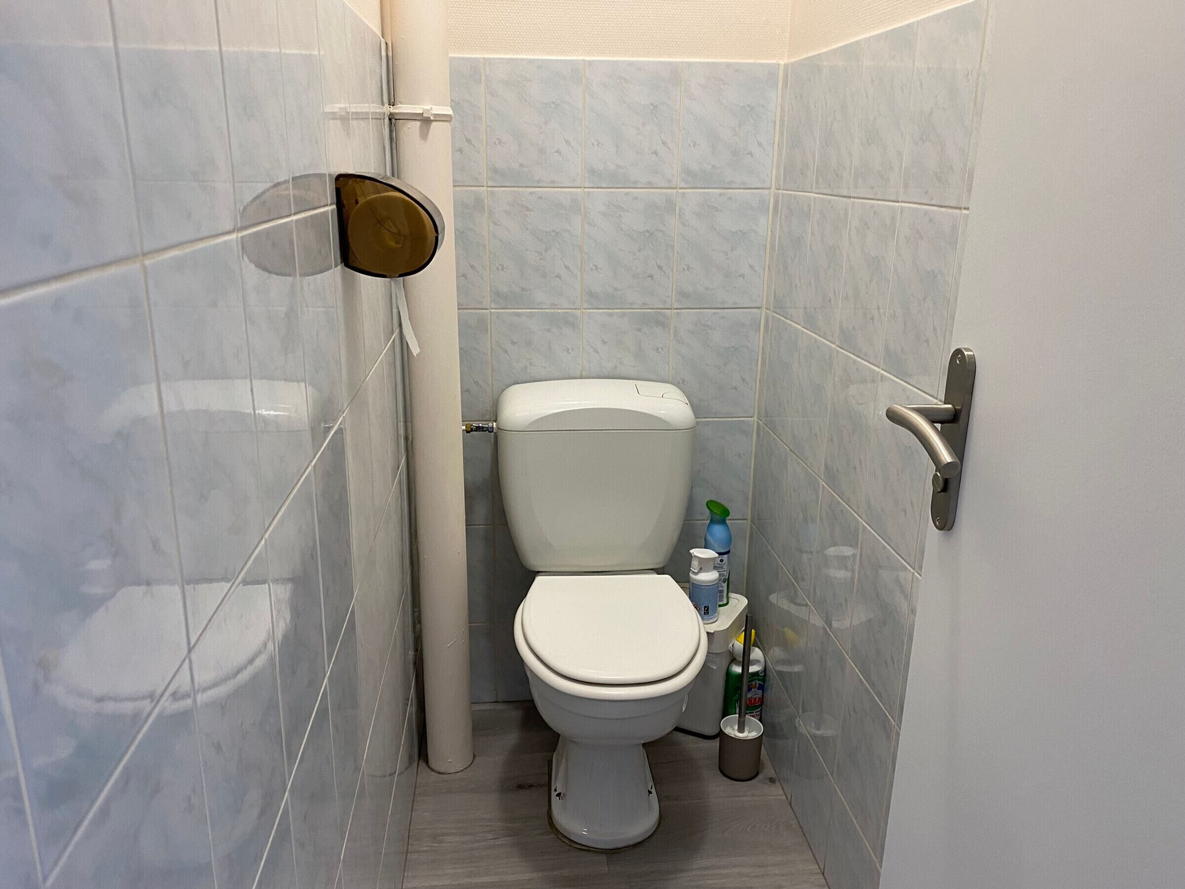 A small, modern bathroom with a toilet, a hand dryer, and a bottle of hand soap on the floor.