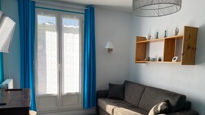 Moderni olohuone, jossa on sohva, koriste-esineillä täytetty puinen hylly ja sinisillä verhoilla varustettu ikkuna.