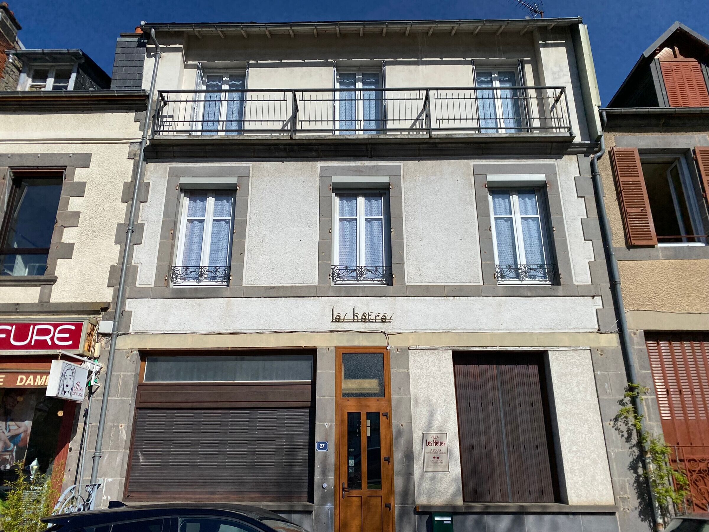 A two-story building with a ground-floor garage, a balcony on the second floor, and a plaque indicating it is a protected historical site.