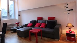 A modern living room with a grey sofa, red cushions, a small red table, and a lamp on a side table. - Bright city-center loft, near thermal baths, for 4 guests (La Bourboule)