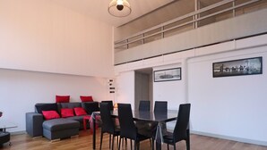 A modern living room with a grey sofa, red cushions, a dining table with chairs, and a cityscape painting on the wall. - Bright city-center loft, near thermal baths, for 4 guests (La Bourboule)