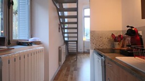 A narrow kitchen with a wooden staircase, white tiled floor, and a red appliance on the counter. - Bright city-center loft, near thermal baths, for 4 guests (La Bourboule)
