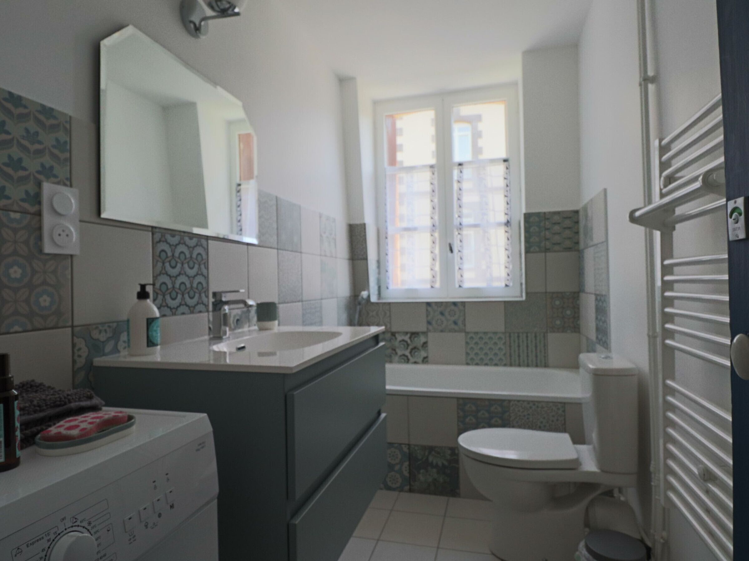 Ein Badezimmer mit Waschbecken, Spiegel, Toilette und Wandfliesen mit Muster.