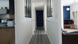 Ein schmaler Flur mit strukturiertem Boden, einer Küche links und einer Sitzecke rechts.