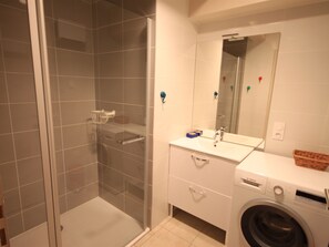 Ein Badezimmer mit einer Duschkabine, einer Waschmaschine von Bosch und einem Waschbecken mit Spiegel.