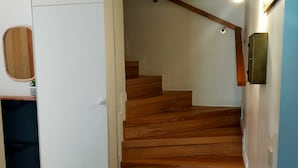 A wooden staircase leading to an upper floor, with a white door on the left and a light fixture on the right. - L'R du Roc: 4* Duplex Apartment with Terrace and Garage (La Bourboule)