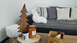 A cozy living room with a wooden Christmas tree, a candle, a jar of honey, and a box of nuts on a wooden coffee table. - L'R du Roc: 4* Duplex Apartment with Terrace and Garage (La Bourboule)