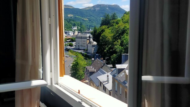A window view of a town with buildings and a mountain in the background. - L'R du Roc: 4* Duplex Apartment with Terrace and Garage (La Bourboule)