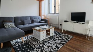Un salon moderne avec un canapé gris, une table basse, un téléviseur posé sur un meuble et un tapis à motifs.