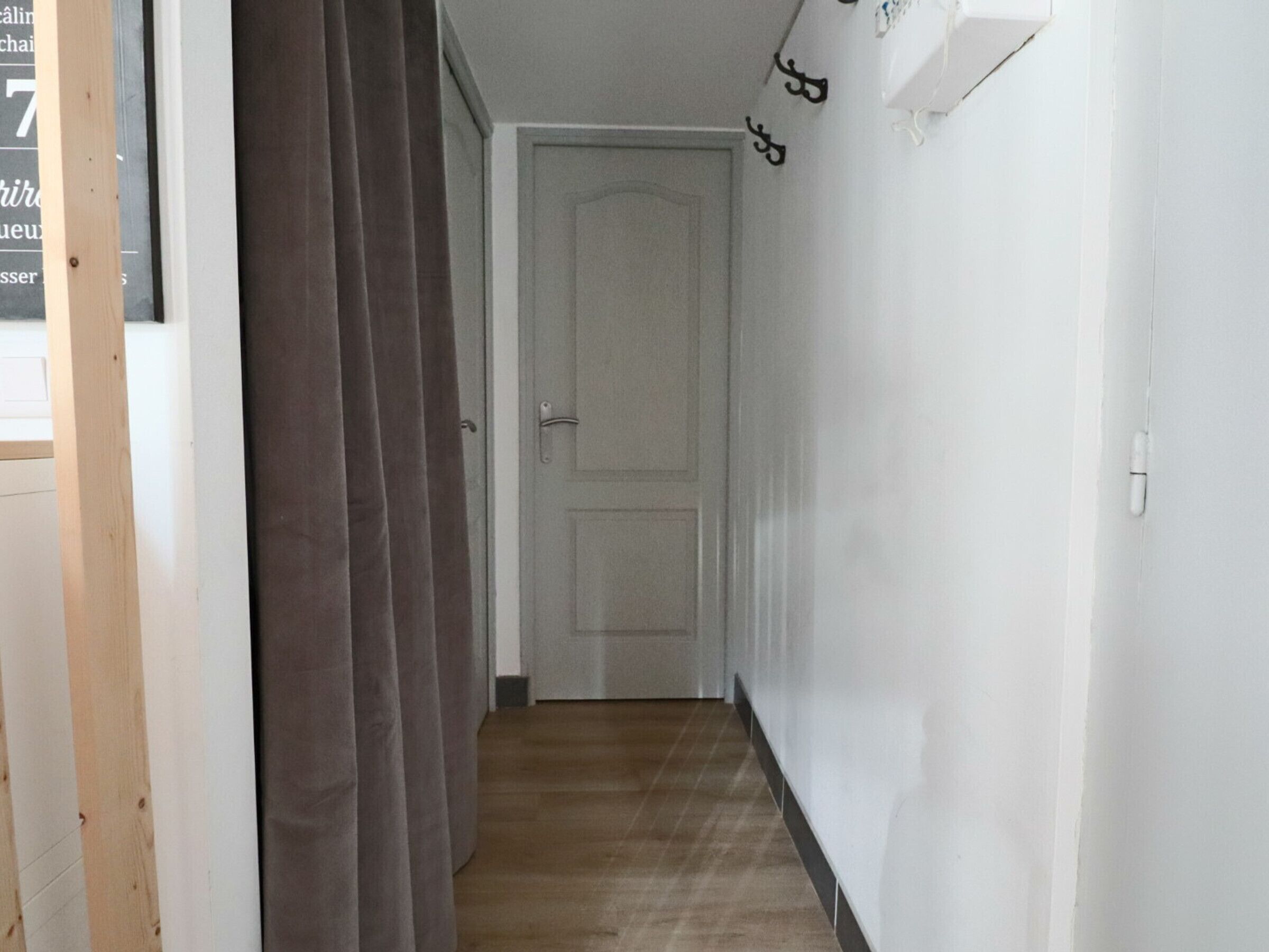 A hallway with a wooden floor, a white door at the end, and a curtain on the left.
