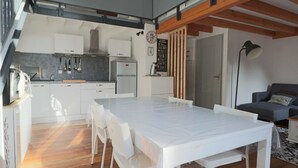 Une cuisine moderne avec des meubles blancs, une grande table à manger et un plafond en bois.