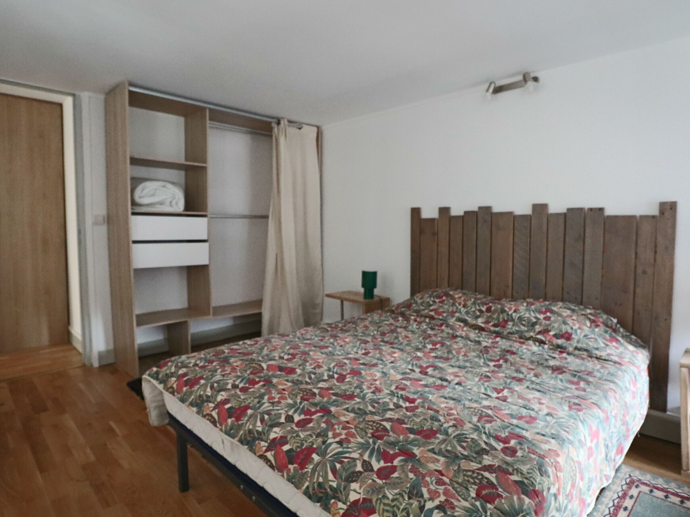 Ein Schlafzimmer mit einem hölzernen Bettgestell, einer blumigen Tagesdecke, einem Holzschrank und einem kleinen Nachttisch.