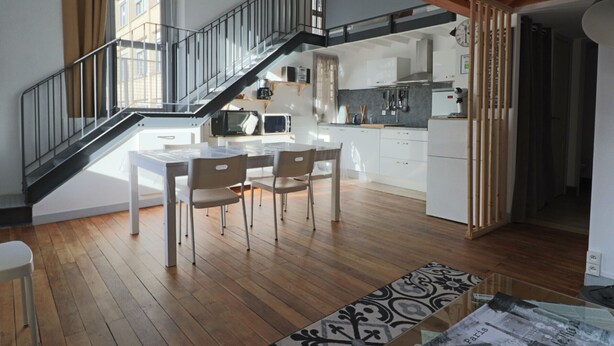 Une cuisine moderne avec un coin repas, un plancher en bois et un escalier menant à un niveau supérieur.