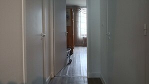Een smalle gang met een houten vloer, witte muren en een deur naar een andere kamer.