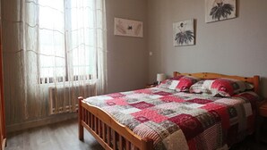 Een slaapkamer met een houten bed, een sprei, een raam met gordijnen en wanddecoratie.