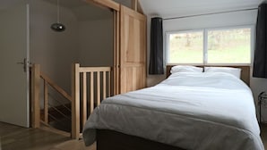 A bedroom with a wooden bed, a window with curtains, a staircase, and a door. - New 4* house in Mont Dore for 6 people (Mont-Dore)