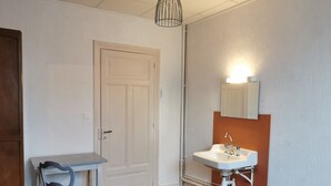 Et lille, kompakt rum med en hvid dør, en hvid vask med et spejl over, og et lille bord med en stol.