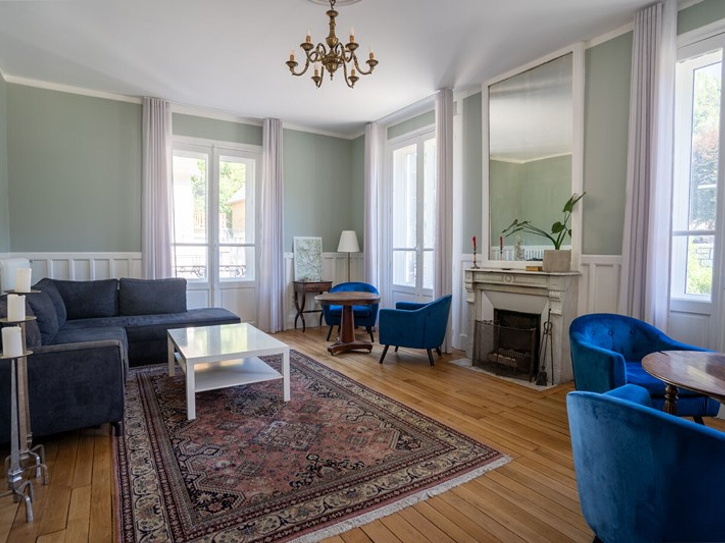 Un salon spacieux avec un grand canapé, deux fauteuils bleus, une table basse et une cheminée.