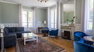 Un salon spacieux avec un grand canapé, deux fauteuils bleus, une table basse et une cheminée.