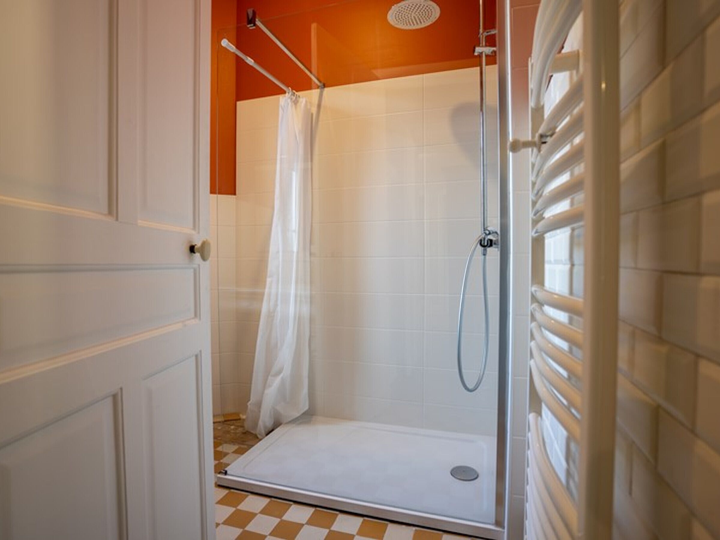 Une douche à l’italienne avec une porte en verre, des murs recouverts de carreaux blancs et un sol à carreaux.