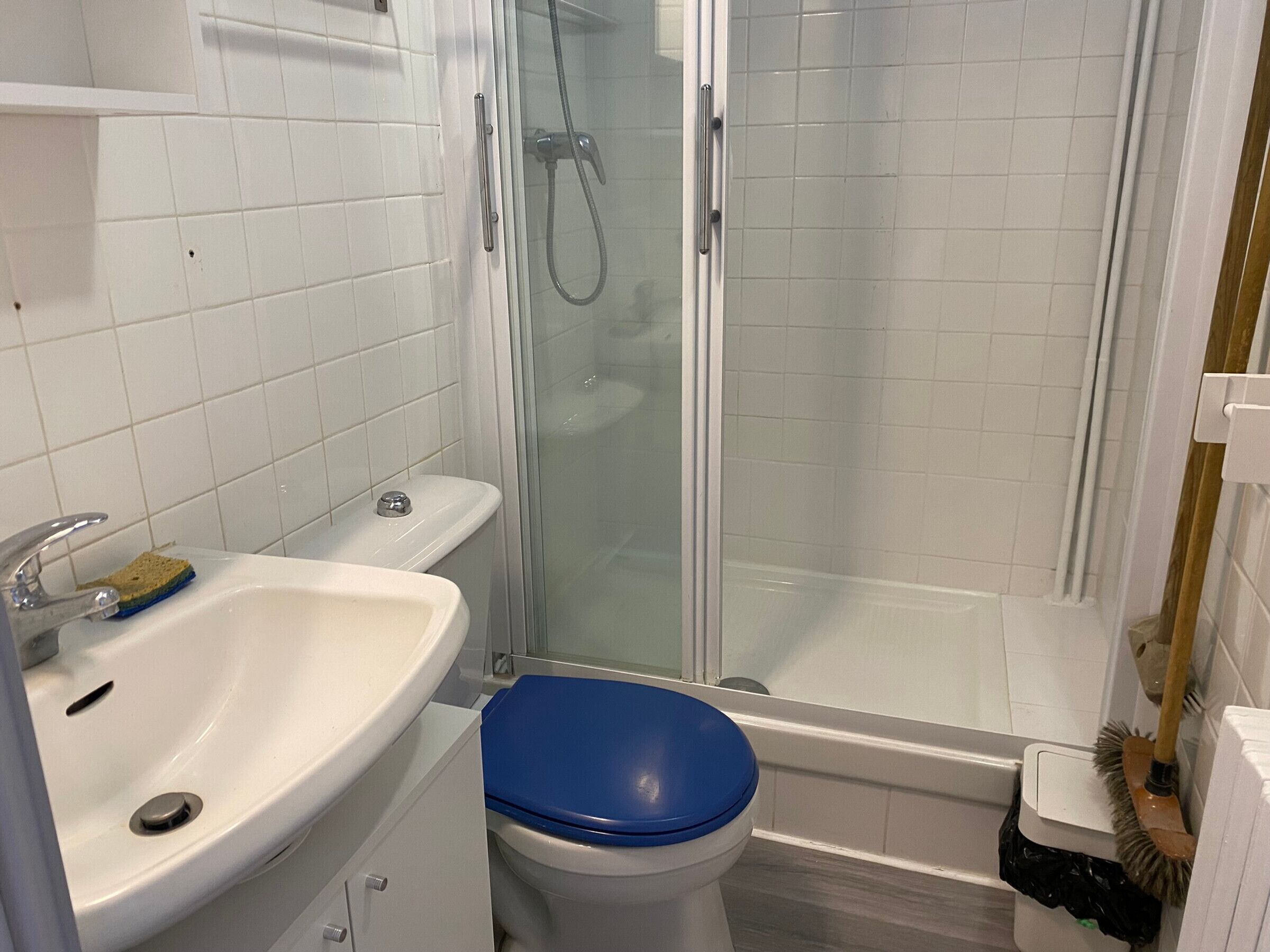 Une salle de bain avec un lavabo blanc, des toilettes bleues et une douche à parois en verre.