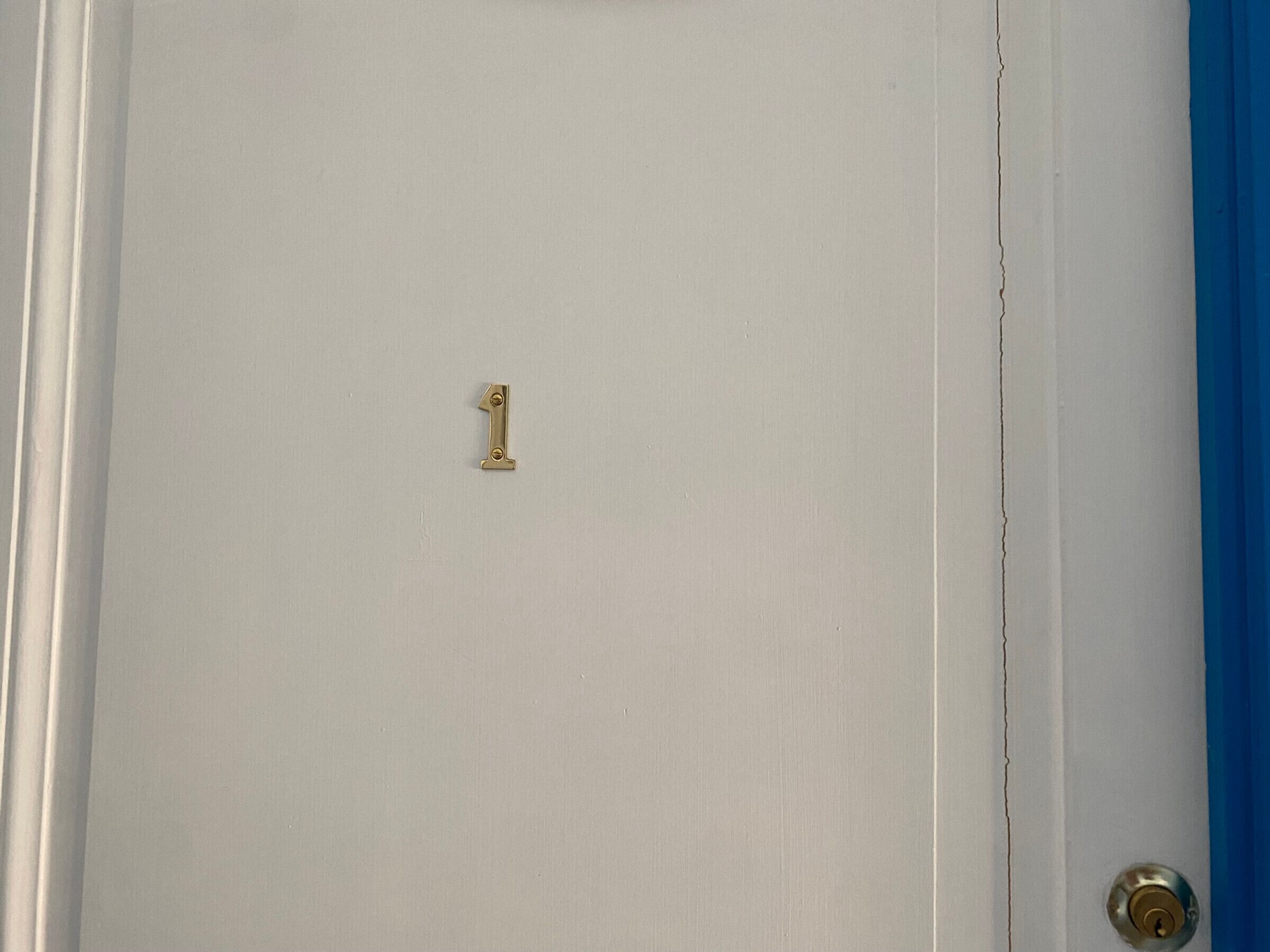 Een witte deur met een messing cijfer '1' slot en een sleutelgat.
