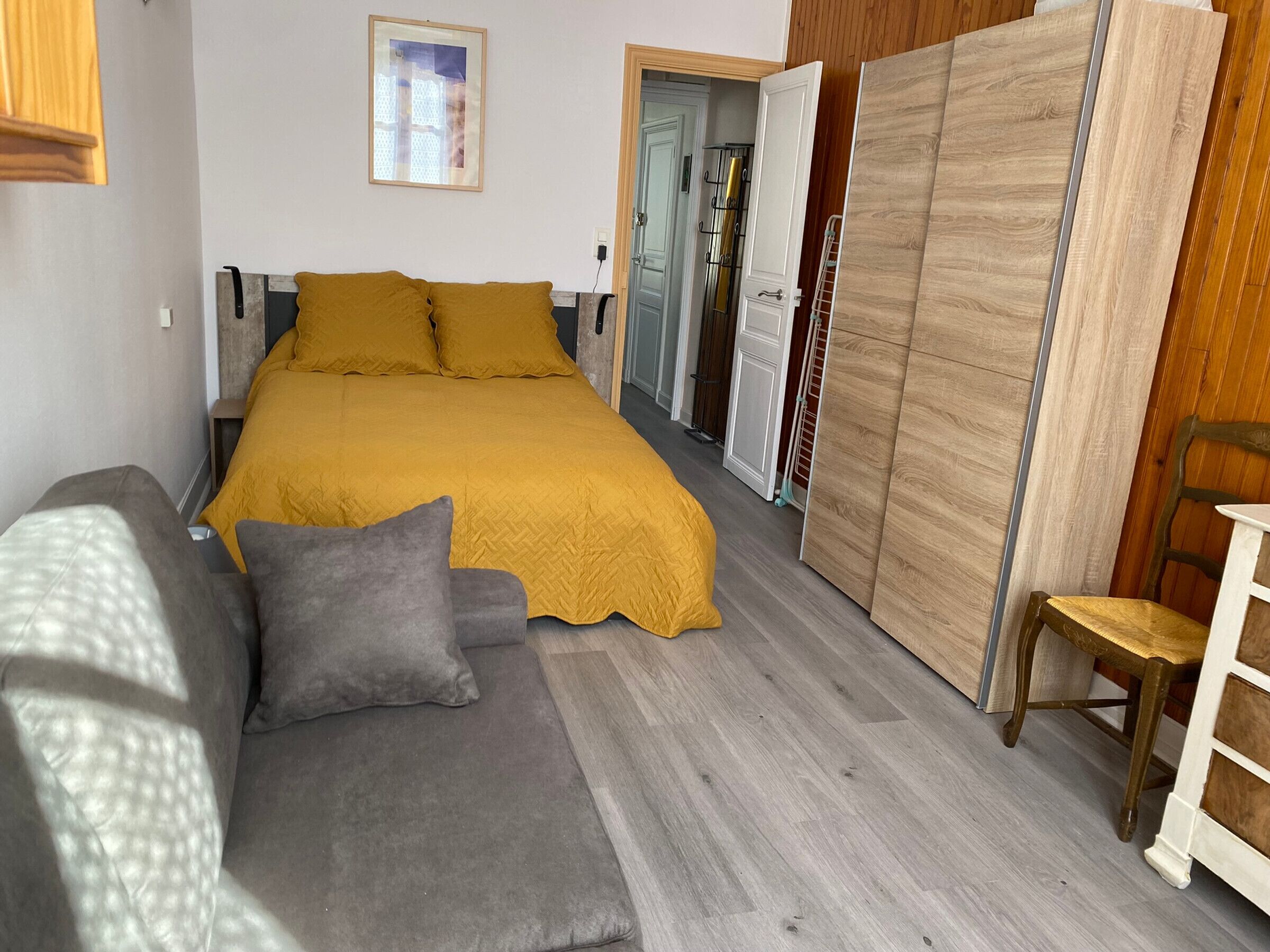 Un dormitorio con cama, sofá gris, armario de madera y una silla.