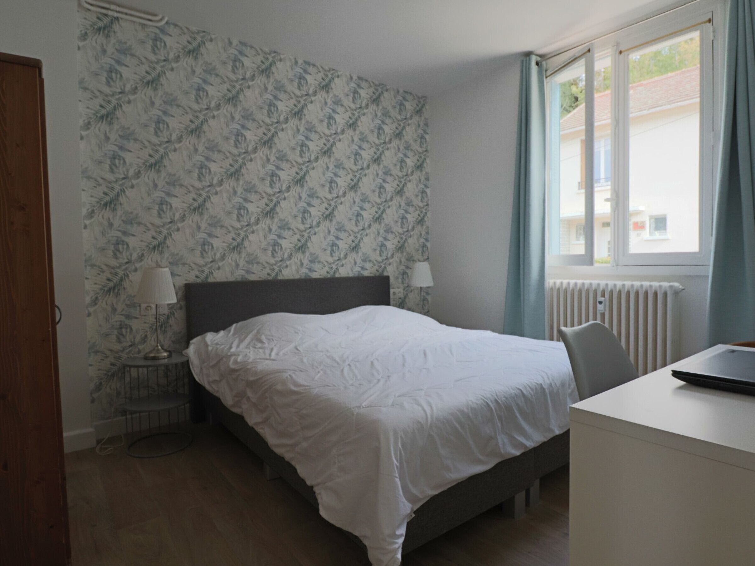 A bedroom with a bed, bedside tables, a desk, and a window with curtains.