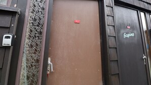 Een bruine deur met een rood bord waarop '5' staat en een keypad aan de linkerkant.