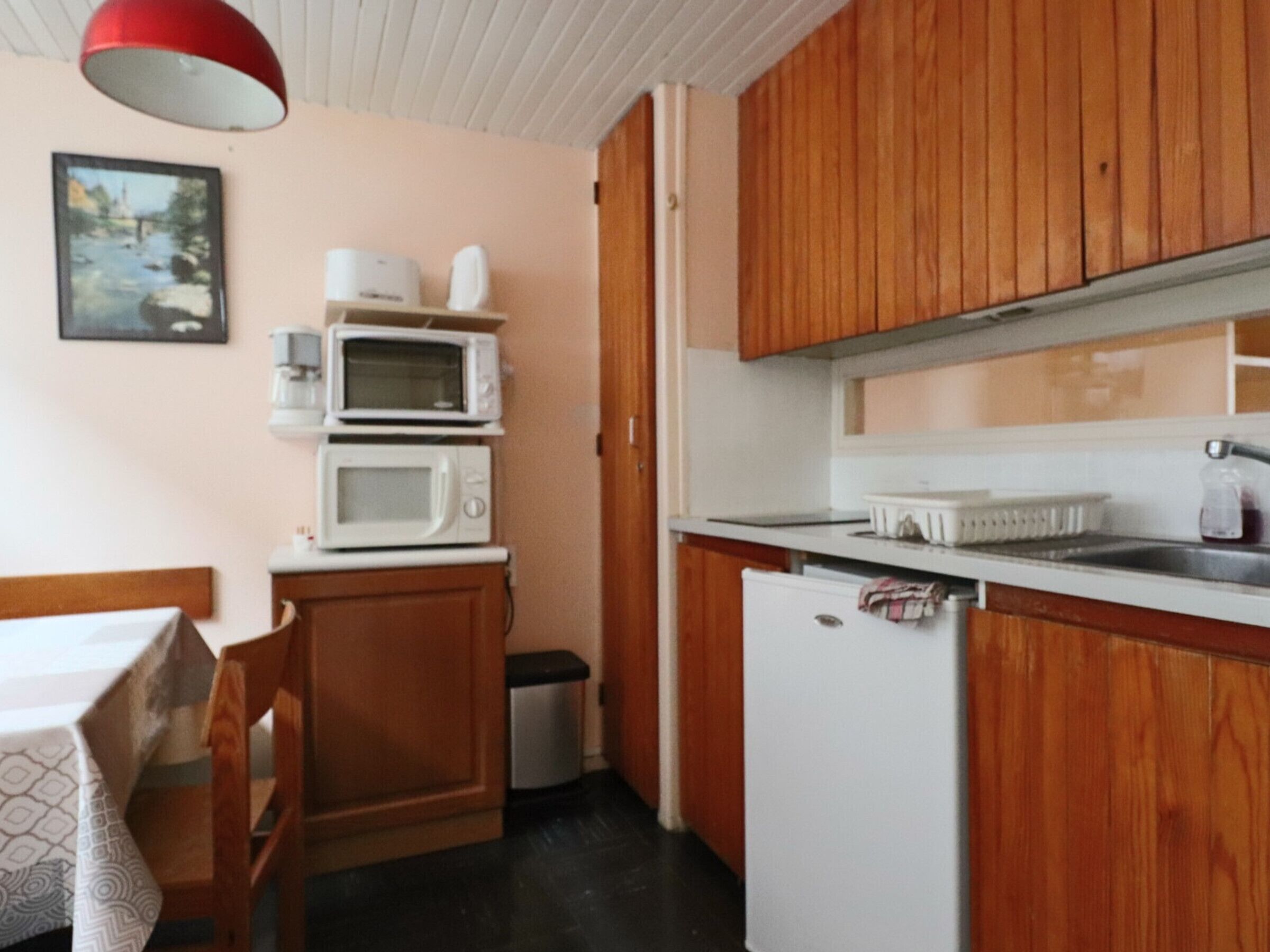 A compact kitchen with wooden cabinets, a white refrigerator, and a microwave stacked on top.