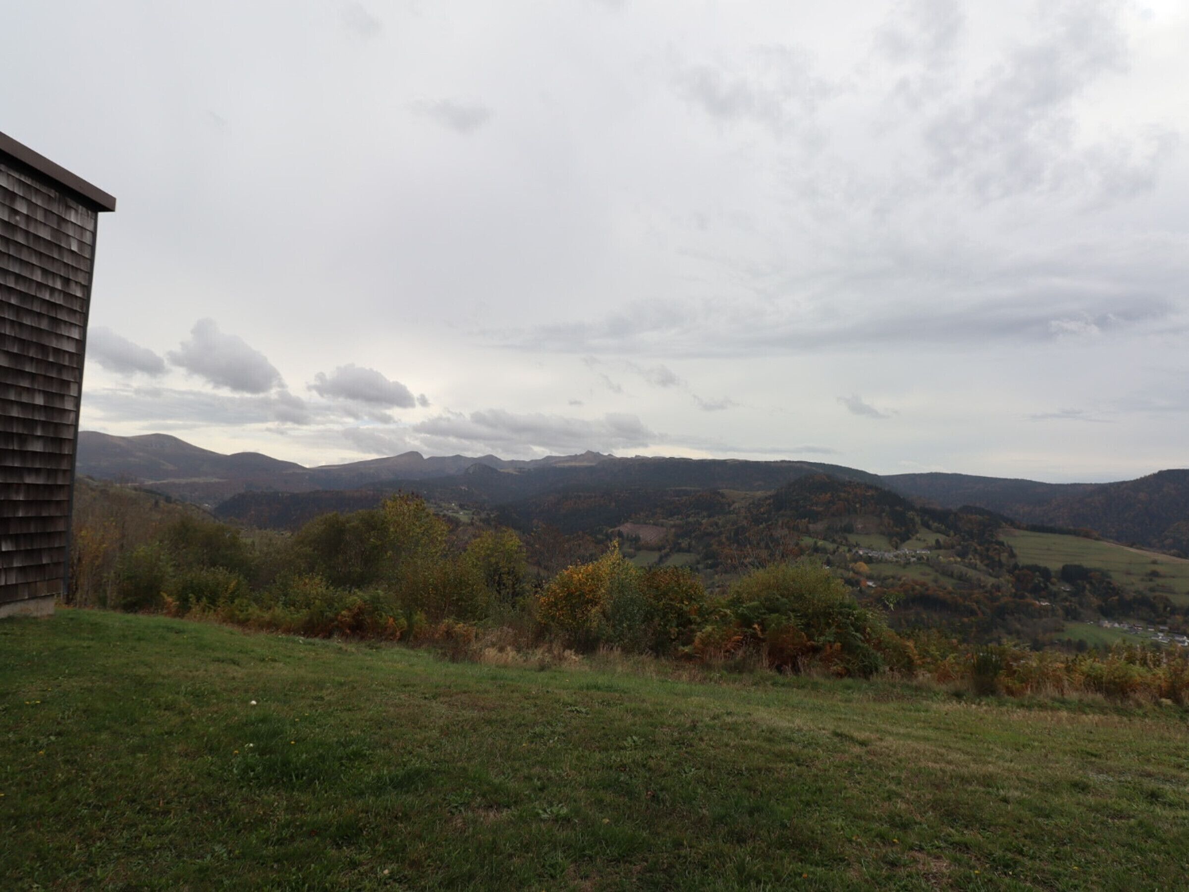 Un paysage rural avec des collines douces et un bâtiment en bois au premier plan.