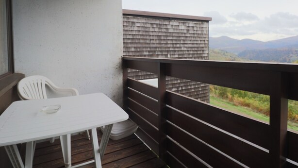 Een balkon met een witte tafel en stoelen, een houten leuning en uitzicht op bergen.