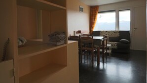 Een woonkamer met een eethoek, een bank en uitzicht op bergen door het raam.