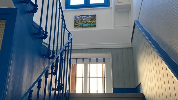 A staircase with blue railings leading to a landing with a window and a painting. - 6-person apartment in La Bourboule center (La Bourboule)