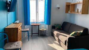 A cozy room with a sofa, a small table, a chair, a TV, and a window with curtains. - 6-person apartment in La Bourboule center (La Bourboule)