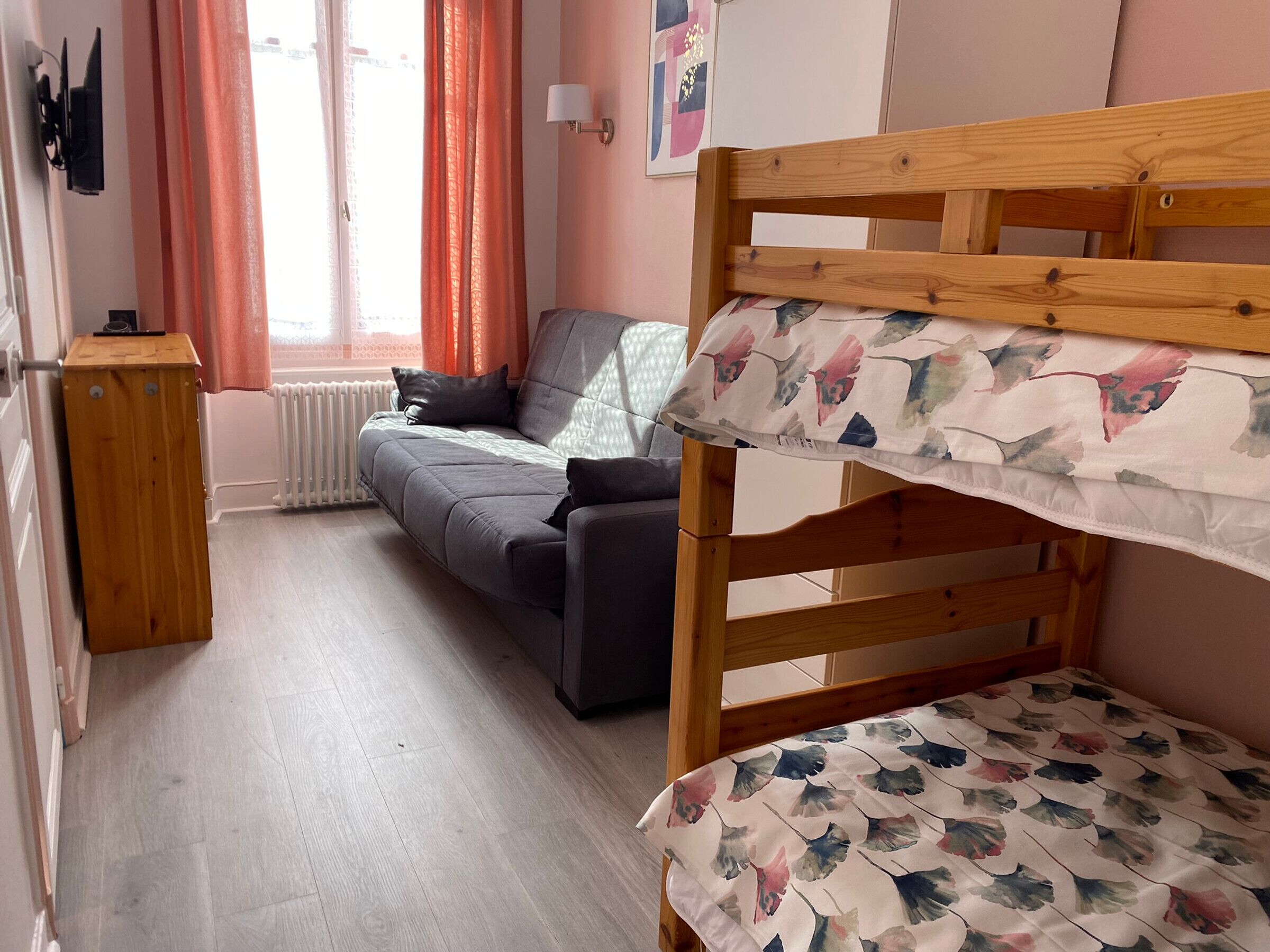 A room with a bunk bed, a sofa, a radiator, a wooden cabinet, and a window with curtains.