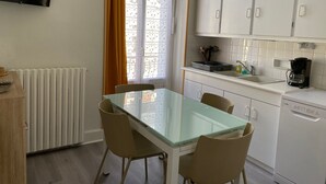 A modern kitchen with white cabinets, a glass-top dining table, and a built-in oven. - 6-person apartment in La Bourboule center (La Bourboule)