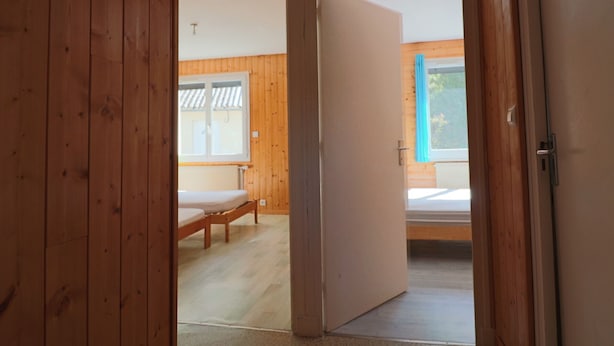 A room with wooden walls, a bed, and a window with a view of greenery.
