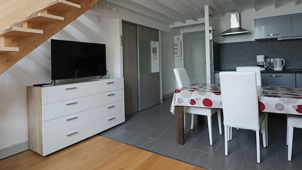 A modern kitchen with a dining area, a TV on a white cabinet, and a staircase. - Cozy duplex in central La Bourboule, up to 6 people (La Bourboule)