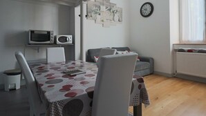 A dining area with a table covered by a polka dot tablecloth, two white chairs, a microwave on a shelf, a gray sofa, and a wall clock. - Cozy duplex in central La Bourboule, up to 6 people (La Bourboule)