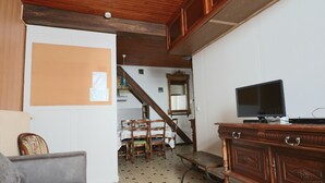 A room with a wooden ceiling, a television on a wooden cabinet, a dining area with chairs and a table, and a staircase leading to another level. - 2* Apartment with private garden, 4 people, in La Bourboule (La Bourboule)