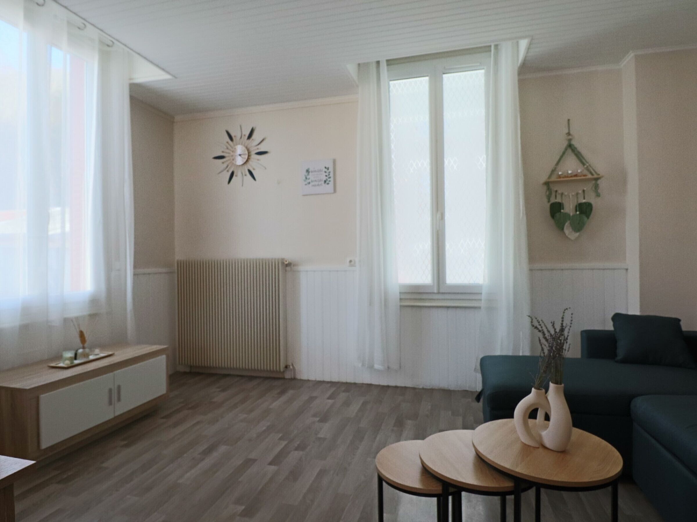 Ein modernes Wohnzimmer mit einem grünen Sofa, zwei runden Holztischen, einem weißen Heizkörper und einer Wanduhr.