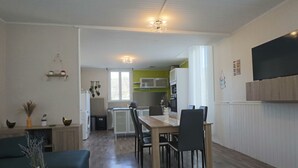 En moderne stue med sofa, sofabord og et spiseområde med bord og stole. Et køkken ses i baggrunden med mikroovn og skabe.