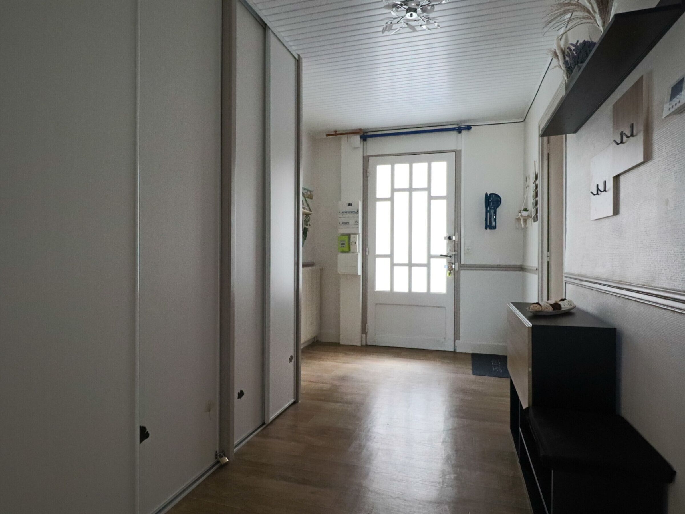 A hallway with a wooden floor, a white door with a window, and a black bench.