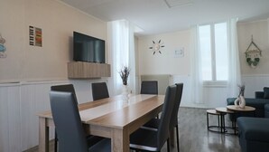 Et moderne spiseområde med et træbord og stole, et fladskærms-tv monteret over, og et hyggeligt siddeområde med en sofa og lænestole.