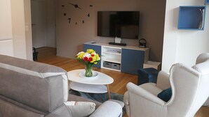 A modern living room with a sofa, armchair, coffee table, and a clock on the wall. - Apartment with large sunny terrace, close to spa and skiing (Mont-Dore)